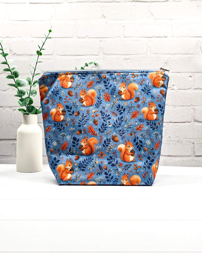 Projekttasche Größe M mit Reißverschluss aus blauem Baumwollstoff mit orangefarbenen Eichhörnchen, Eicheln und Blättern zur Aufbewahrung von Wolle und Strickprojekten. Handgenäht in Bayern von Nadelmikado.