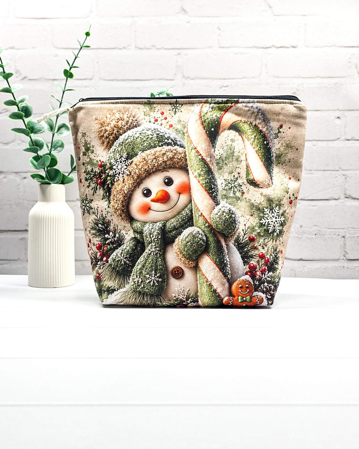 Projekttasche Isvind Größe M mit fröhlichem Schneemann in grüner Strickmütze und Schal, großer grün-weißer Zuckerstange, Schneeflocken und winterlichen Tannenzweigen. Mit Reißverschluss für Strickprojekte bis 400 g Wolle. Handgenäht in Bayern von Nadelmikado.