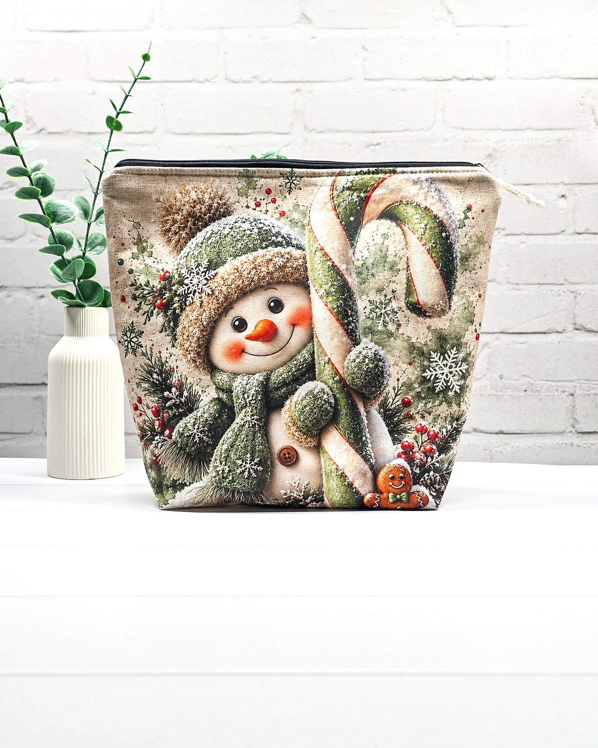 Projekttasche Isvind Größe M mit fröhlichem Schneemann in grüner Strickmütze und Schal, großer grün-weißer Zuckerstange, Schneeflocken und winterlichen Tannenzweigen. Mit Reißverschluss für Strickprojekte bis 400 g Wolle. Handgenäht in Bayern von Nadelmikado.