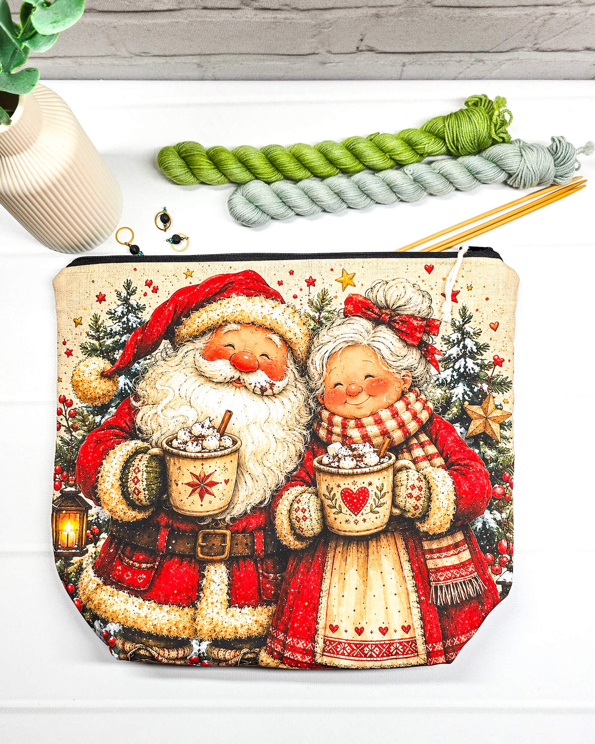 Projekttasche Isvind Größe M mit fröhlichem Weihnachtsmann und Weihnachtsfrau in rot-weißer Winterkleidung, heißen Kakaotassen, Tannenbäumen und Weihnachtssternen. Mit Reißverschluss für Strickprojekte bis 400 g Wolle. Handgenäht in Bayern von Nadelmikado.