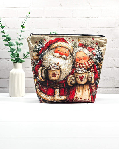 Projekttasche Isvind Größe M mit fröhlichem Weihnachtsmann und Weihnachtsfrau in rot-weißer Winterkleidung, heißen Kakaotassen, Tannenbäumen und Weihnachtssternen. Mit Reißverschluss für Strickprojekte bis 400 g Wolle. Handgenäht in Bayern von Nadelmikado.