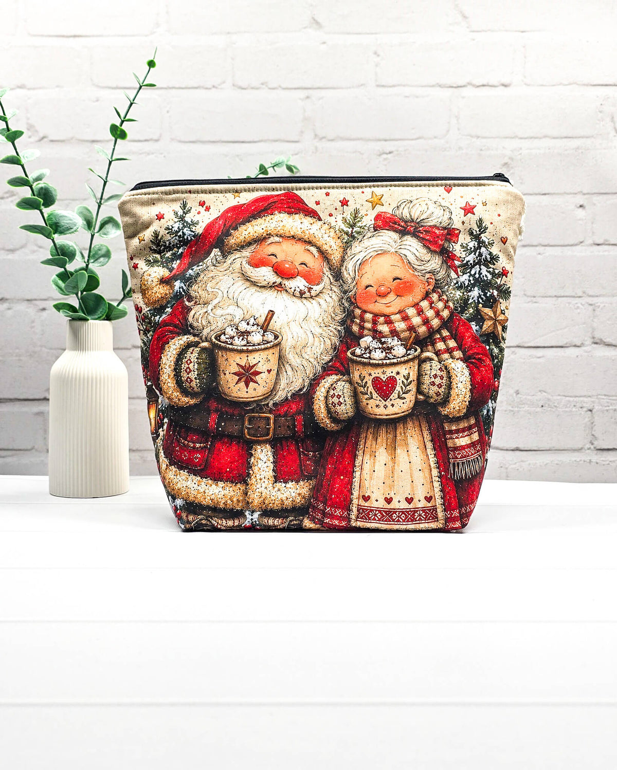 Projekttasche Isvind Größe M mit fröhlichem Weihnachtsmann und Weihnachtsfrau in rot-weißer Winterkleidung, heißen Kakaotassen, Tannenbäumen und Weihnachtssternen. Mit Reißverschluss für Strickprojekte bis 400 g Wolle. Handgenäht in Bayern von Nadelmikado.