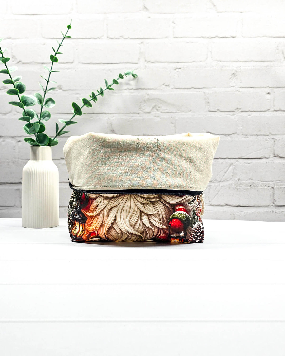 Projekttasche Isvind Größe M mit Weihnachtswichtel, rot-grüner Zipfelmütze, langem weißem Bart, verschneiten Tannen und leuchtenden Laternen. Mit Reißverschluss für Strickprojekte bis 400 g Wolle. Handgenäht in Bayern von Nadelmikado.