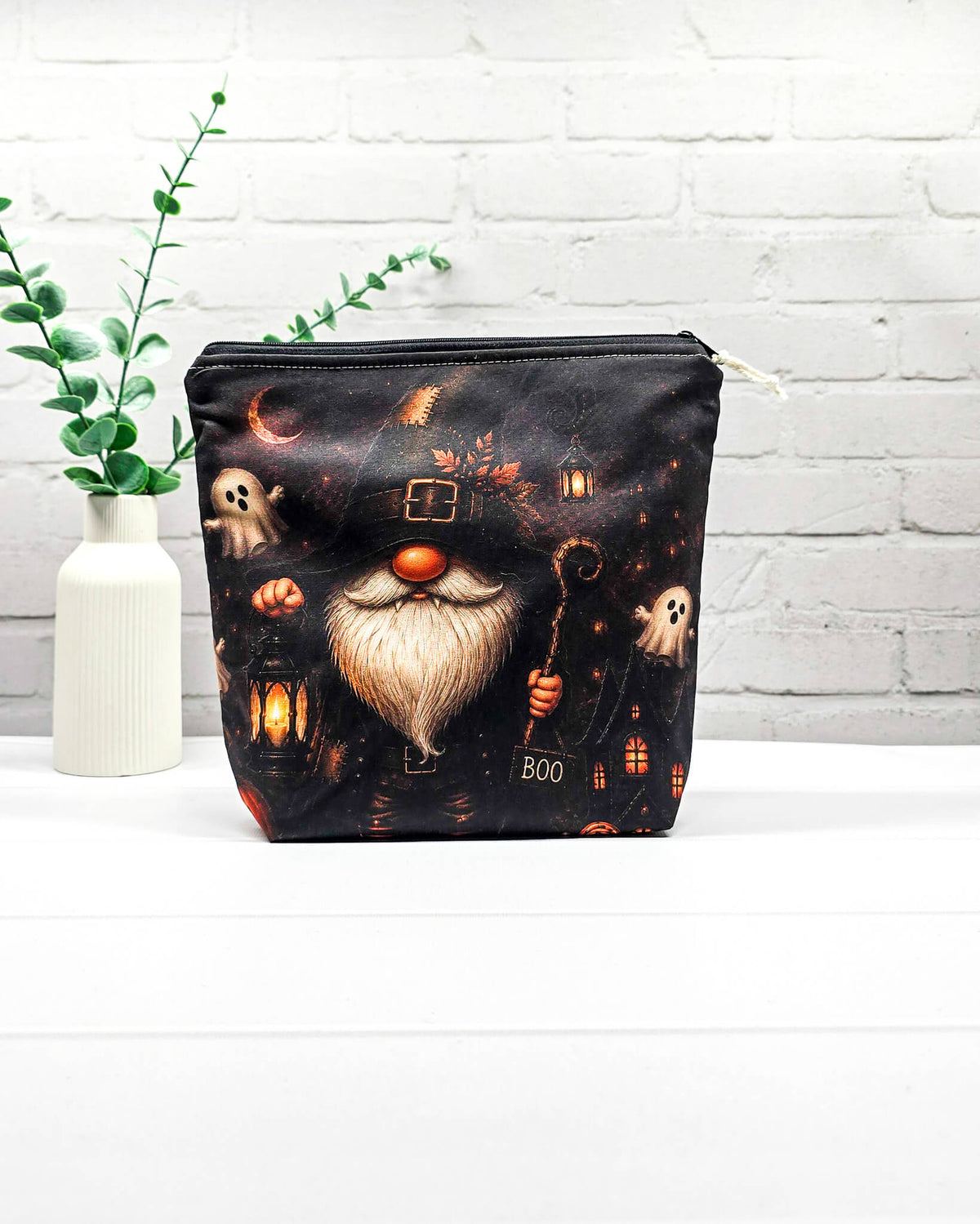 Projekttasche Isvind Größe S mit Halloweenwichtel in schwarzem Hexenhut, weißem Bart, leuchtender Laterne und kleinen Gespenstern vor dunkler Häuserkulisse. Stricktasche mit Reißverschluss für kleine Strickprojekte. Handgenäht in Bayern von Nadelmikado.