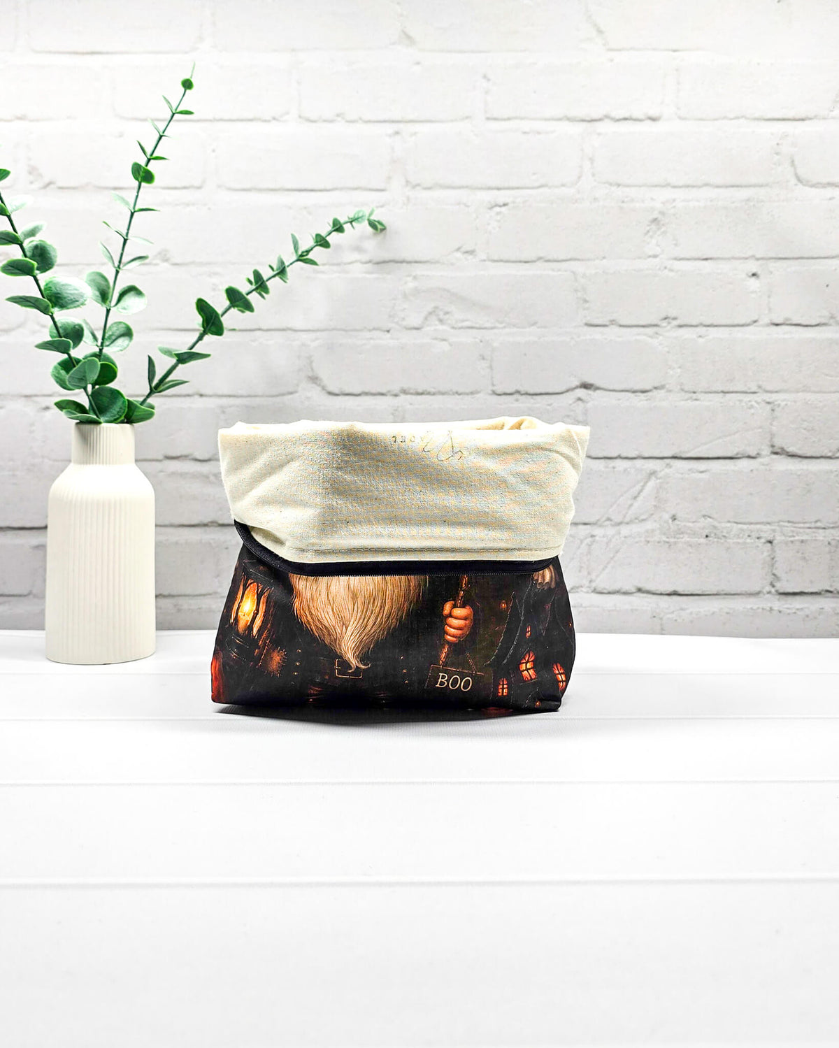 Projekttasche Isvind Größe S mit Halloweenwichtel in schwarzem Hexenhut, weißem Bart, leuchtender Laterne und kleinen Gespenstern vor dunkler Häuserkulisse. Stricktasche mit Reißverschluss für kleine Strickprojekte. Handgenäht in Bayern von Nadelmikado.