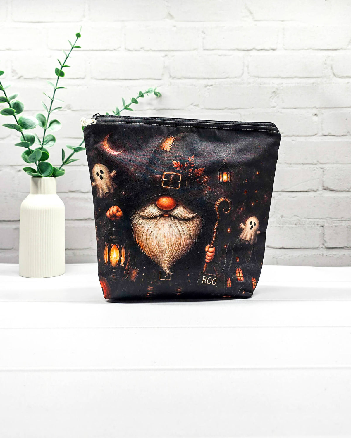 Projekttasche Isvind Größe S mit Halloweenwichtel in schwarzem Hexenhut, weißem Bart, leuchtender Laterne und kleinen Gespenstern vor dunkler Häuserkulisse. Stricktasche mit Reißverschluss für kleine Strickprojekte. Handgenäht in Bayern von Nadelmikado.