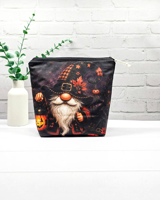 Projekttasche Isvind Größe S mit Halloweenwichtel, schwarzer Zipfelmütze, weißem Bart und leuchtender Kürbislaterne auf dunklem Hintergrund. Mit Reißverschluss für kleine Strickprojekte. Handgenäht in Bayern von Nadelmikado.