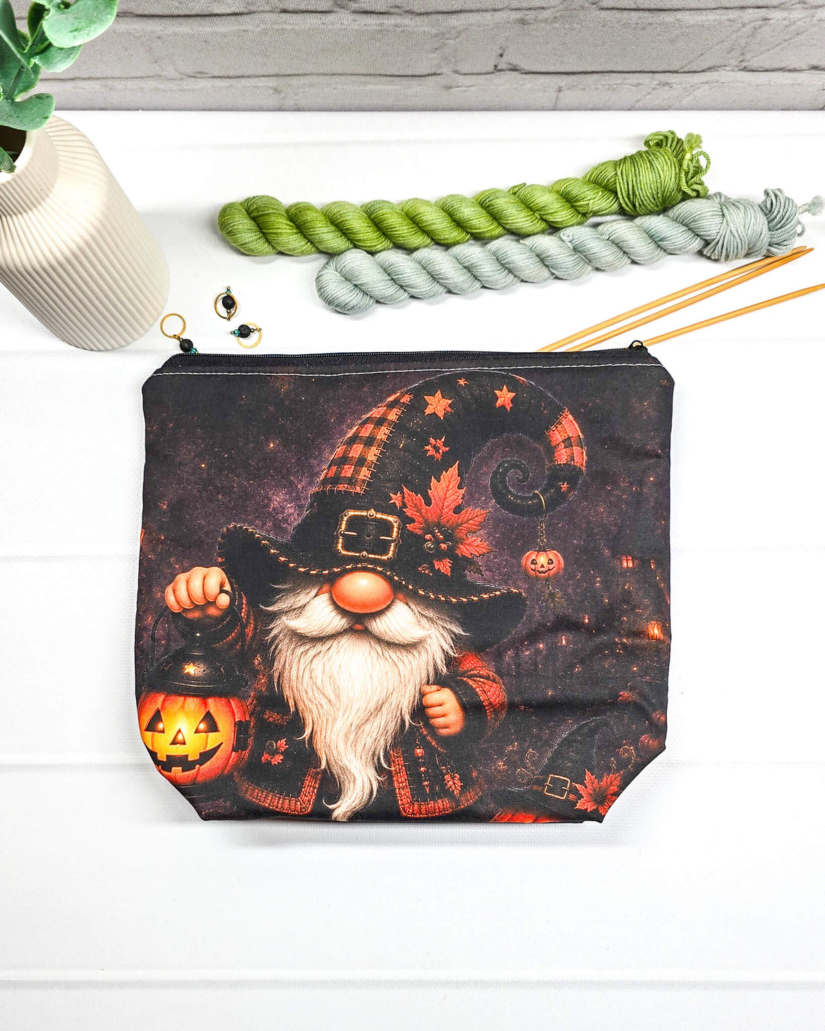 Projekttasche Isvind Größe S mit Halloweenwichtel, schwarzer Zipfelmütze, weißem Bart und leuchtender Kürbislaterne auf dunklem Hintergrund. Mit Reißverschluss für kleine Strickprojekte. Handgenäht in Bayern von Nadelmikado.