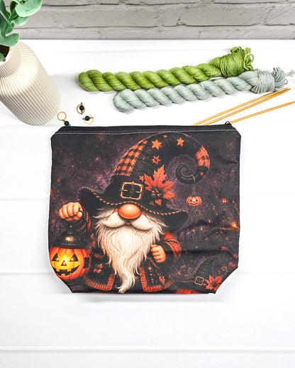 Projekttasche Isvind Größe S mit Halloweenwichtel, schwarzer Zipfelmütze, weißem Bart und leuchtender Kürbislaterne auf dunklem Hintergrund. Mit Reißverschluss für kleine Strickprojekte. Handgenäht in Bayern von Nadelmikado.