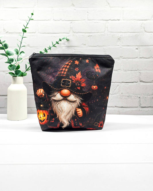 Projekttasche Isvind Größe S mit Halloweenwichtel, schwarzer Zipfelmütze, weißem Bart und leuchtender Kürbislaterne auf dunklem Hintergrund. Mit Reißverschluss für kleine Strickprojekte. Handgenäht in Bayern von Nadelmikado.