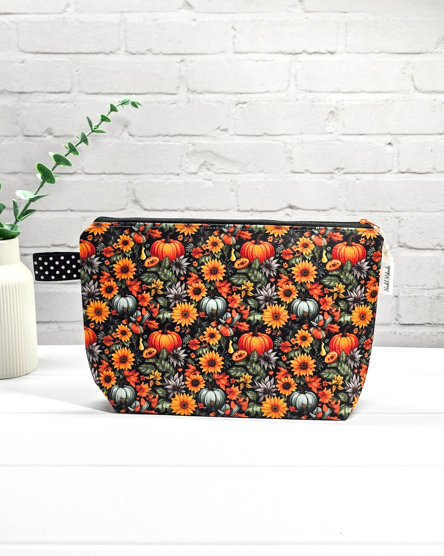 Handgefertigte Projekttasche Isvind S mit Kürbis-Print und Sonnenblumen, kleine Zubehörtasche für Wolle und Strickzeug vor weißer Ziegelwand. Handgenäht in Bayern von Nadelmikado