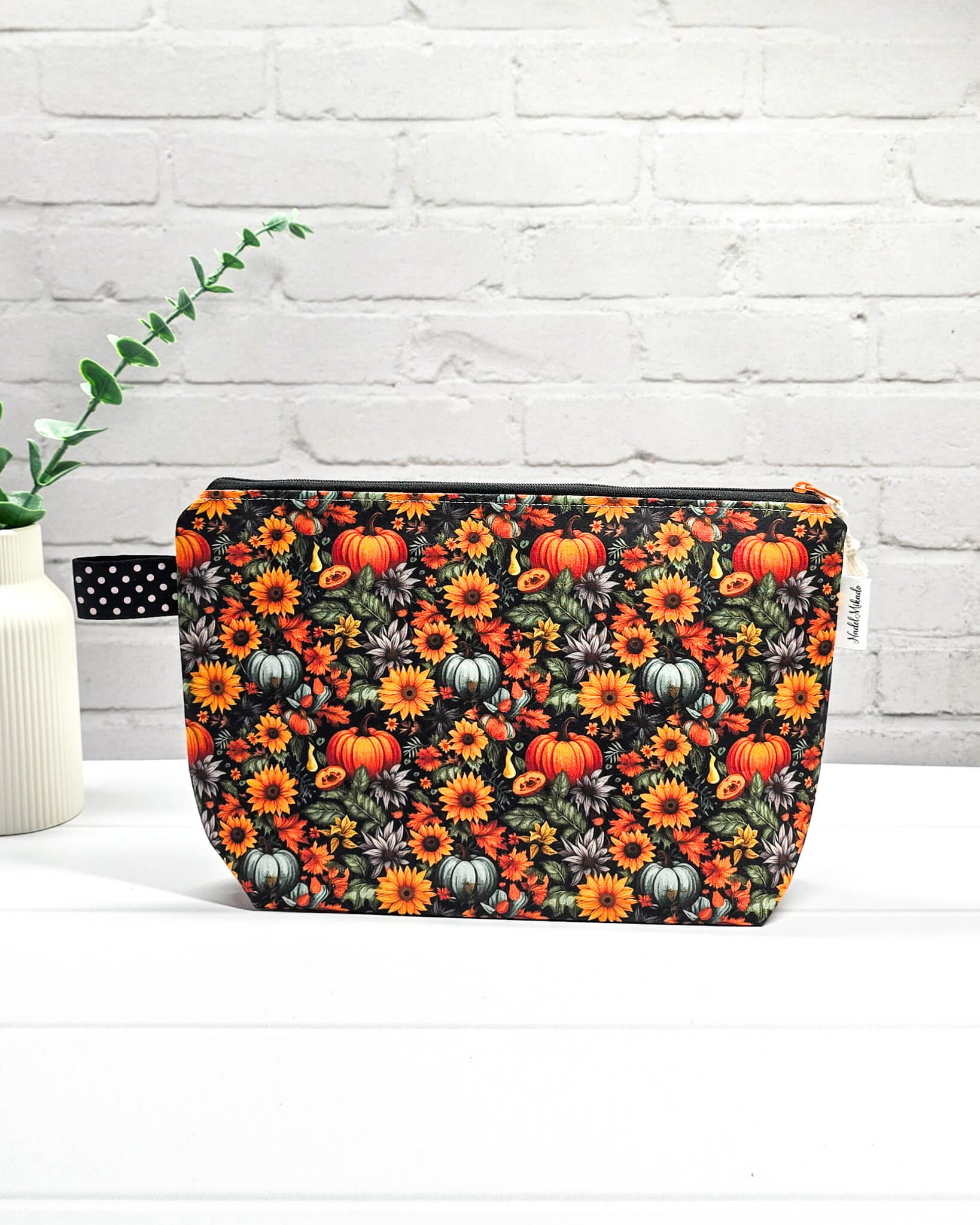 Handgefertigte Projekttasche Isvind S mit Kürbis-Print und Sonnenblumen, kleine Zubehörtasche für Wolle und Strickzeug vor weißer Ziegelwand. Handgenäht in Bayern von Nadelmikado