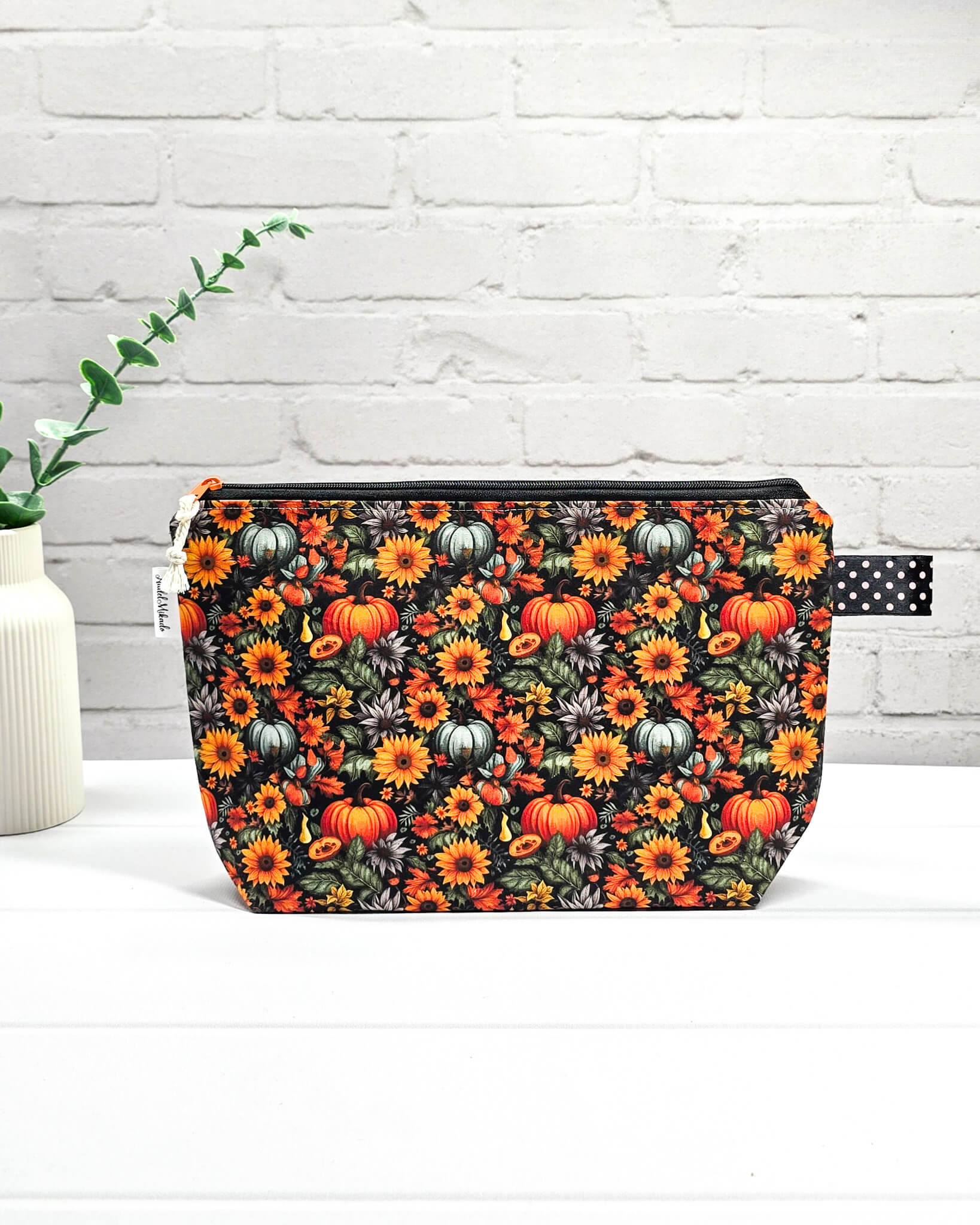 Handgefertigte Projekttasche Isvind S mit Kürbis-Print und Sonnenblumen, kleine Zubehörtasche für Wolle und Strickzeug vor weißer Ziegelwand. Handgenäht in Bayern von Nadelmikado