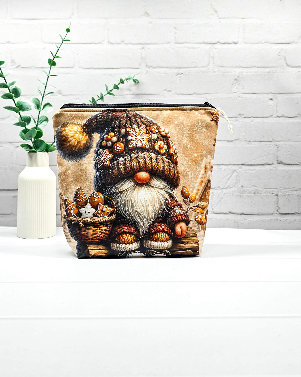Projekttasche Isvind Größe S mit Weihnachtswichtel, brauner Strickmütze mit Lebkuchenverzierungen, weißem Bart und einem Korb voller Lebkuchen vor verschneiten Häuschen. Mit Reißverschluss für kleine Strickprojekte. Handgenäht in Bayern von Nadelmikado.