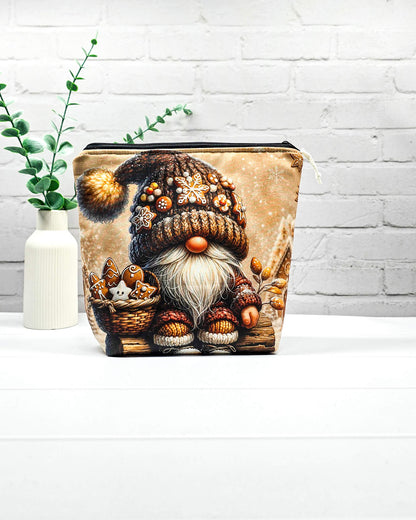 Projekttasche Isvind Größe S mit Weihnachtswichtel, brauner Strickmütze mit Lebkuchenverzierungen, weißem Bart und einem Korb voller Lebkuchen vor verschneiten Häuschen. Mit Reißverschluss für kleine Strickprojekte. Handgenäht in Bayern von Nadelmikado.