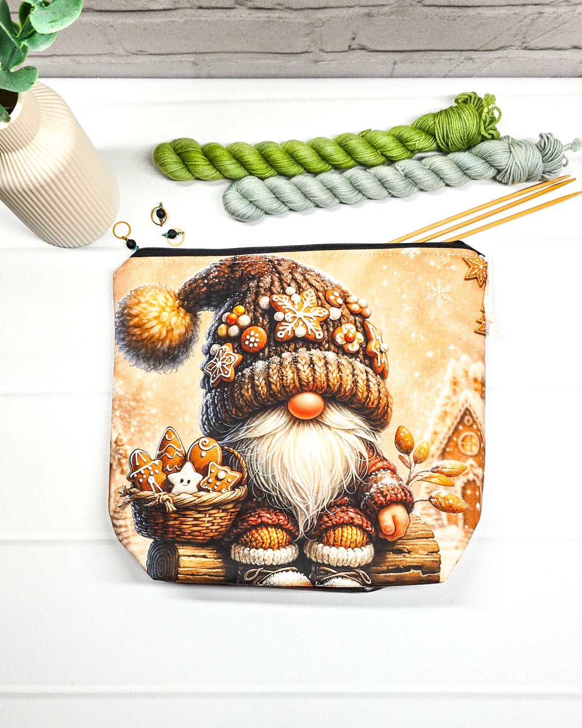 Projekttasche Isvind Größe S mit Weihnachtswichtel, brauner Strickmütze mit Lebkuchenverzierungen, weißem Bart und einem Korb voller Lebkuchen vor verschneiten Häuschen. Mit Reißverschluss für kleine Strickprojekte. Handgenäht in Bayern von Nadelmikado.