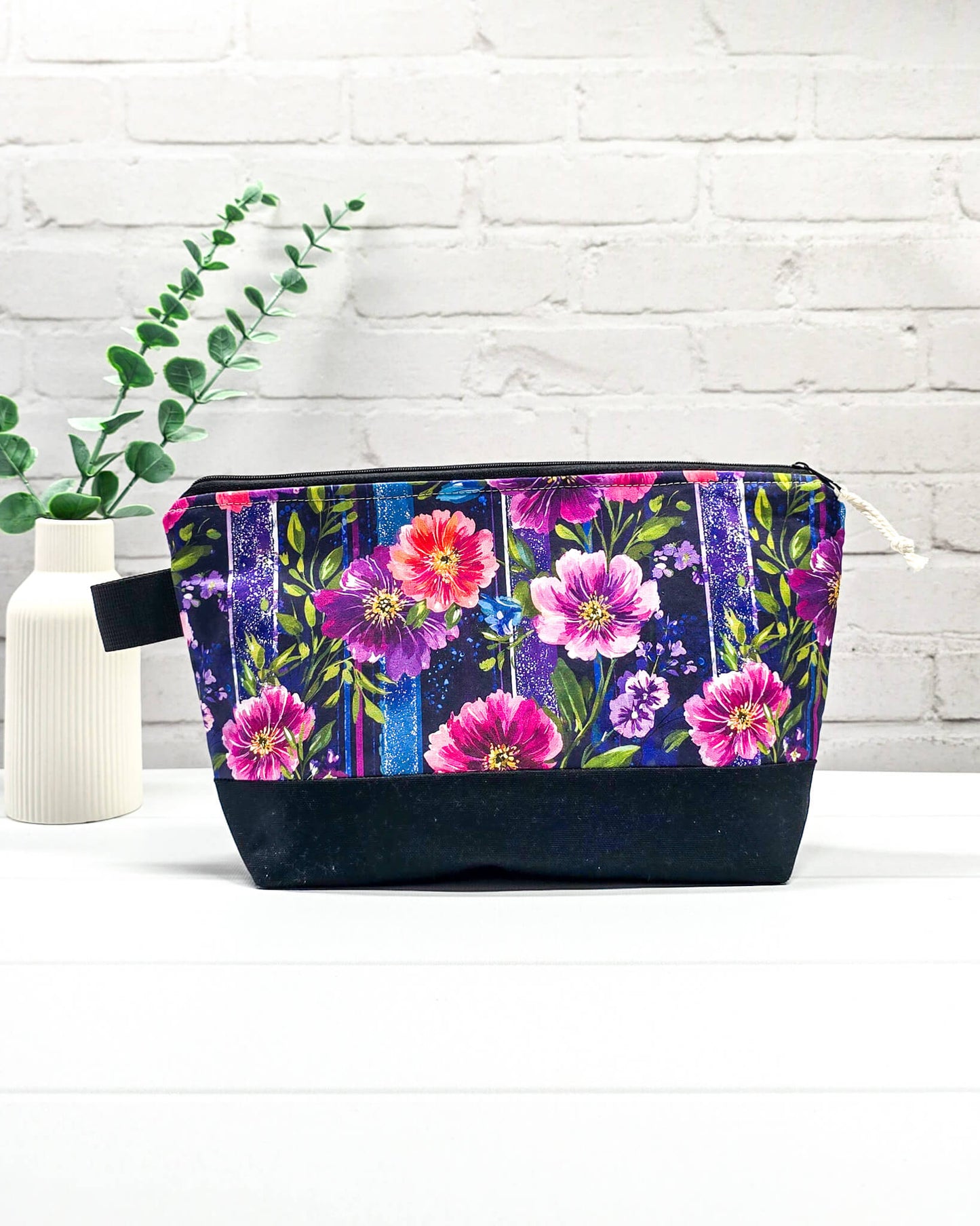 Stricktasche mit pink-violettem Blütenmuster auf Streifendekor, schwarzem Canvas-Boden und Reißverschluss. Platz für 200g Wolle. Handgenäht in Bayern von Nadelmikado.