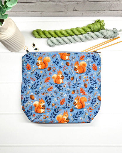 Projekttasche Größe S mit Reißverschluss aus blauem Baumwollstoff mit orangefarbenen Eichhörnchen, Eicheln und Waldzweigen zur Aufbewahrung kleiner Strickprojekte. Handgenäht in Bayern von Nadelmikado.