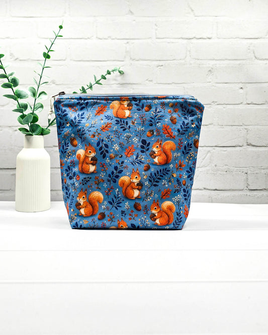 Projekttasche Größe S mit Reißverschluss aus blauem Baumwollstoff mit orangefarbenen Eichhörnchen, Eicheln und Waldzweigen zur Aufbewahrung kleiner Strickprojekte. Handgenäht in Bayern von Nadelmikado.