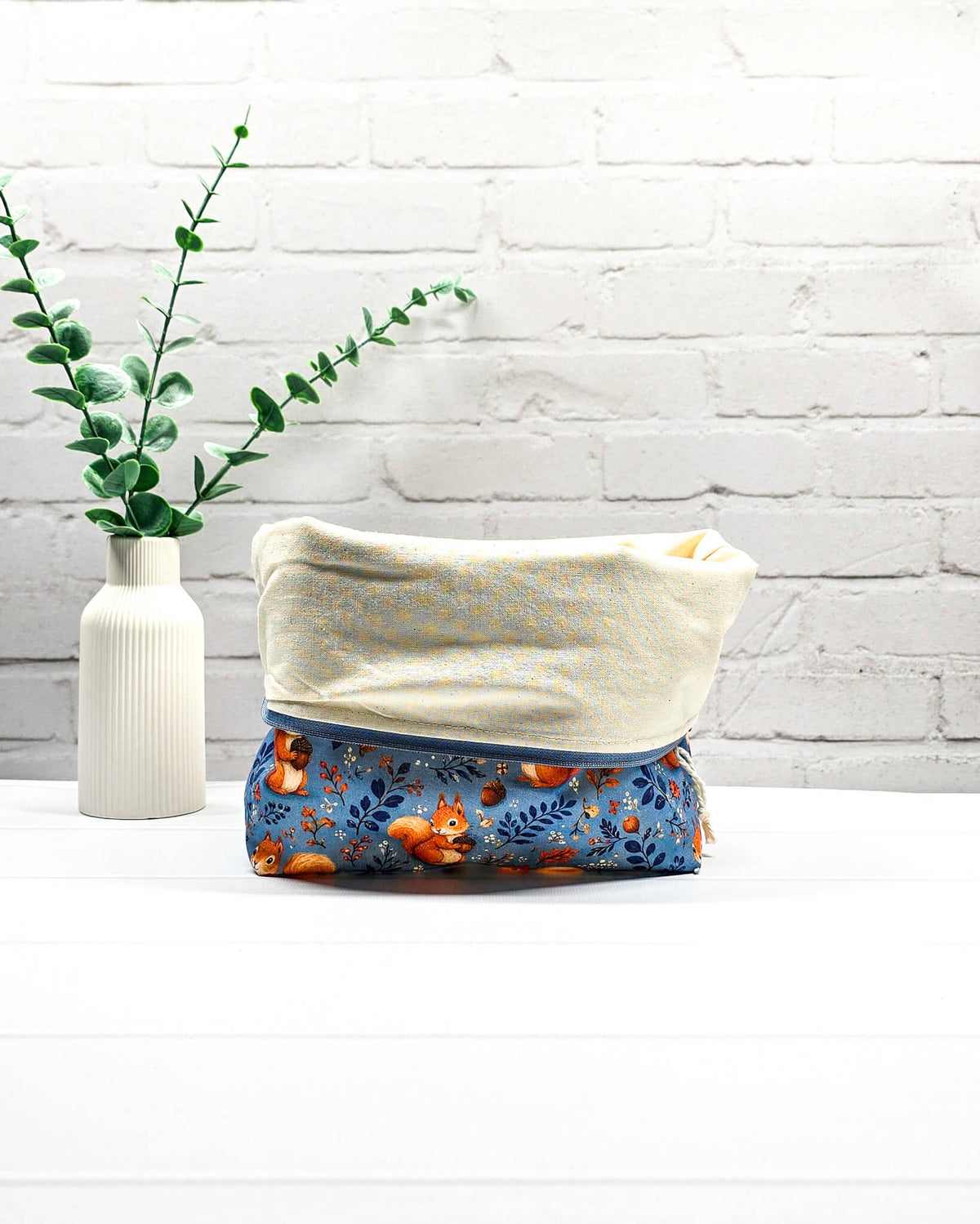 Projekttasche Größe S mit Reißverschluss aus blauem Baumwollstoff mit orangefarbenen Eichhörnchen, Eicheln und Waldzweigen zur Aufbewahrung kleiner Strickprojekte. Handgenäht in Bayern von Nadelmikado.