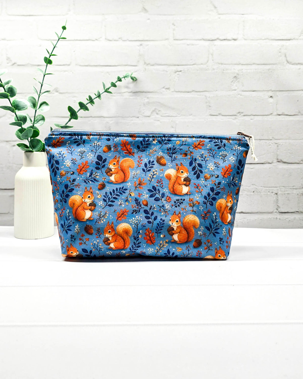 Kleine Projekttasche mit Reißverschluss aus blauem Baumwollstoff mit orangefarbenen Eichhörnchen, Eicheln und Blättern. Handgenäht in Bayern von Nadelmikado.