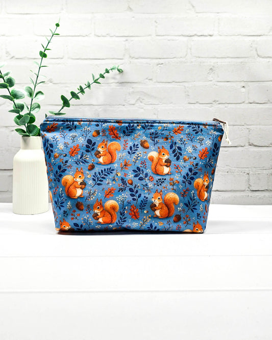 Kleine Projekttasche mit Reißverschluss aus blauem Baumwollstoff mit orangefarbenen Eichhörnchen, Eicheln und Blättern. Handgenäht in Bayern von Nadelmikado.