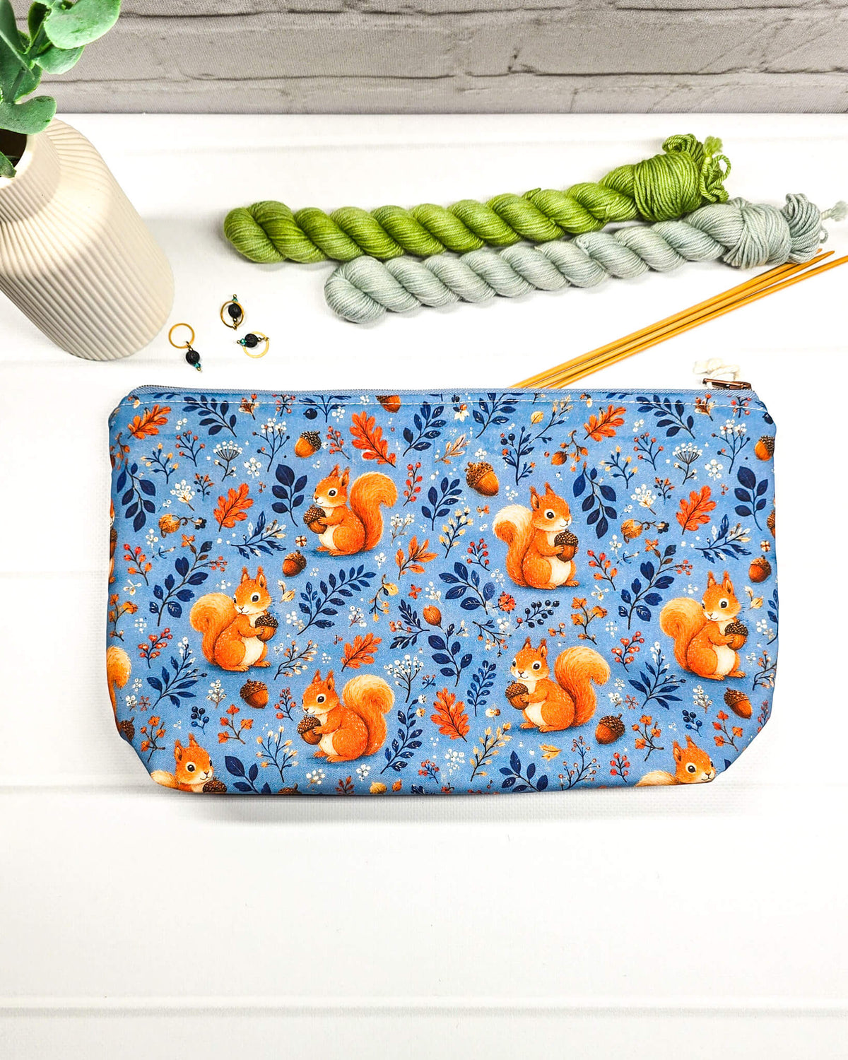 Kleine Projekttasche mit Reißverschluss aus blauem Baumwollstoff mit orangefarbenen Eichhörnchen, Eicheln und Blättern. Handgenäht in Bayern von Nadelmikado.