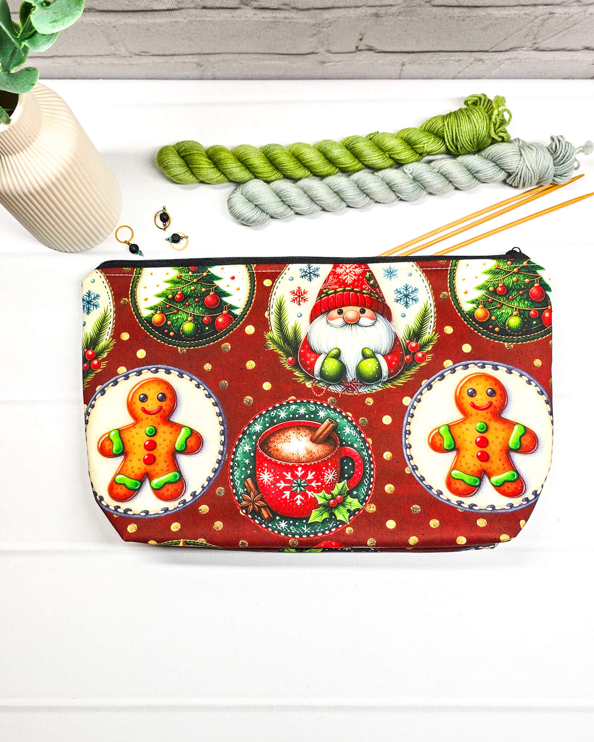 Projekttasche Isvind Größe S mit Weihnachtswichtel, Lebkuchenmännchen, geschmückten Tannenbäumen und roter Tasse auf dunkelrotem Stoff mit goldenen Punkten. Mit Reißverschluss für Strickprojekte bis 200 g Wolle. Handgenäht in Bayern von Nadelmikado.