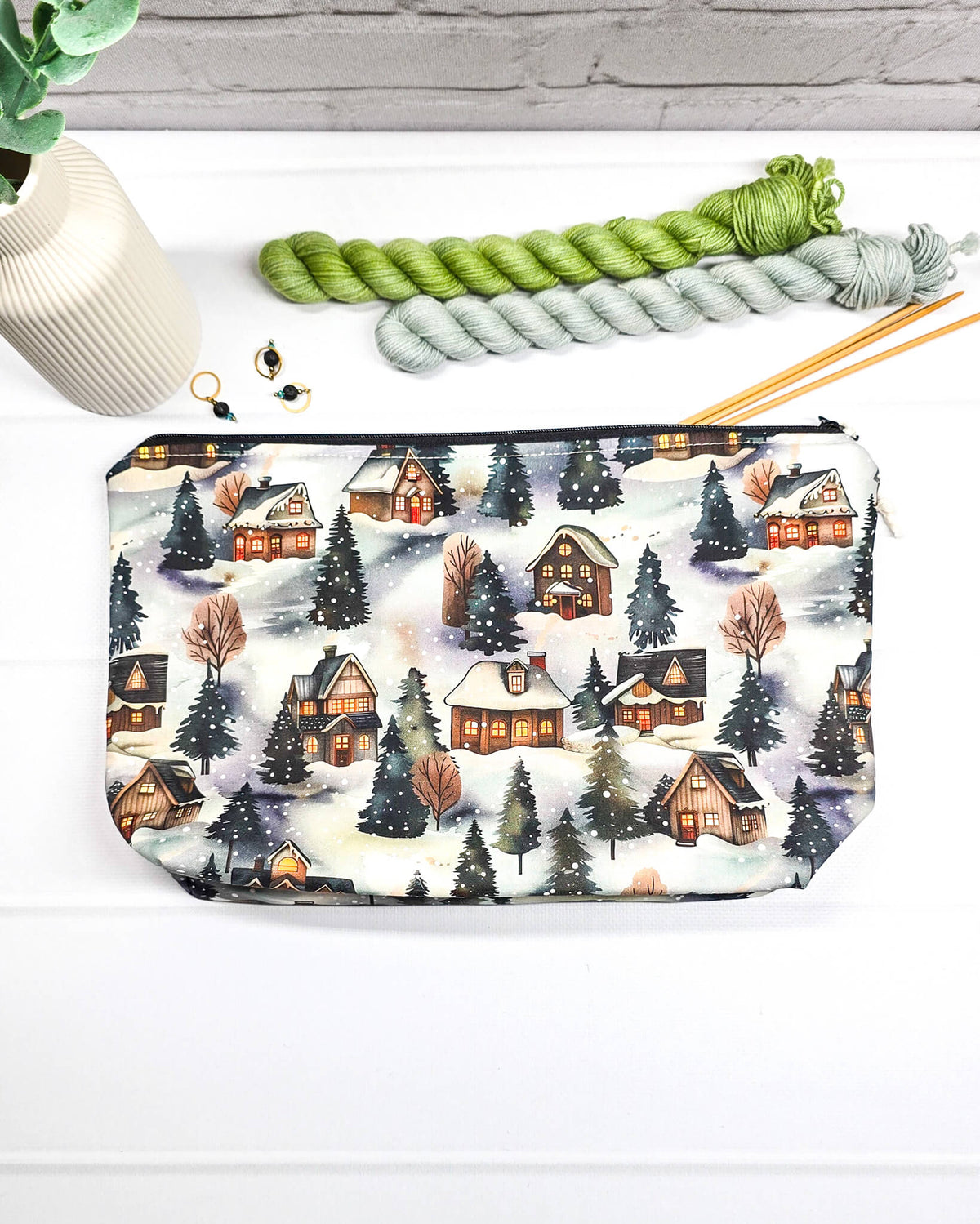 Projekttasche Isvind Größe S mit verschneiten Winterhäusern, leuchtenden Fenstern und dunklen Tannenbäumen auf winterlichem Stoff. Mit Reißverschluss für kleine Strickprojekte. Handgenäht in Bayern von Nadelmikado.