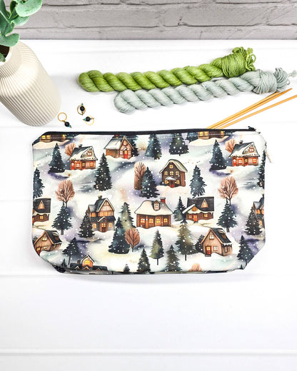 Projekttasche Isvind Größe S mit verschneiten Winterhäusern, leuchtenden Fenstern und dunklen Tannenbäumen auf winterlichem Stoff. Mit Reißverschluss für kleine Strickprojekte. Handgenäht in Bayern von Nadelmikado.