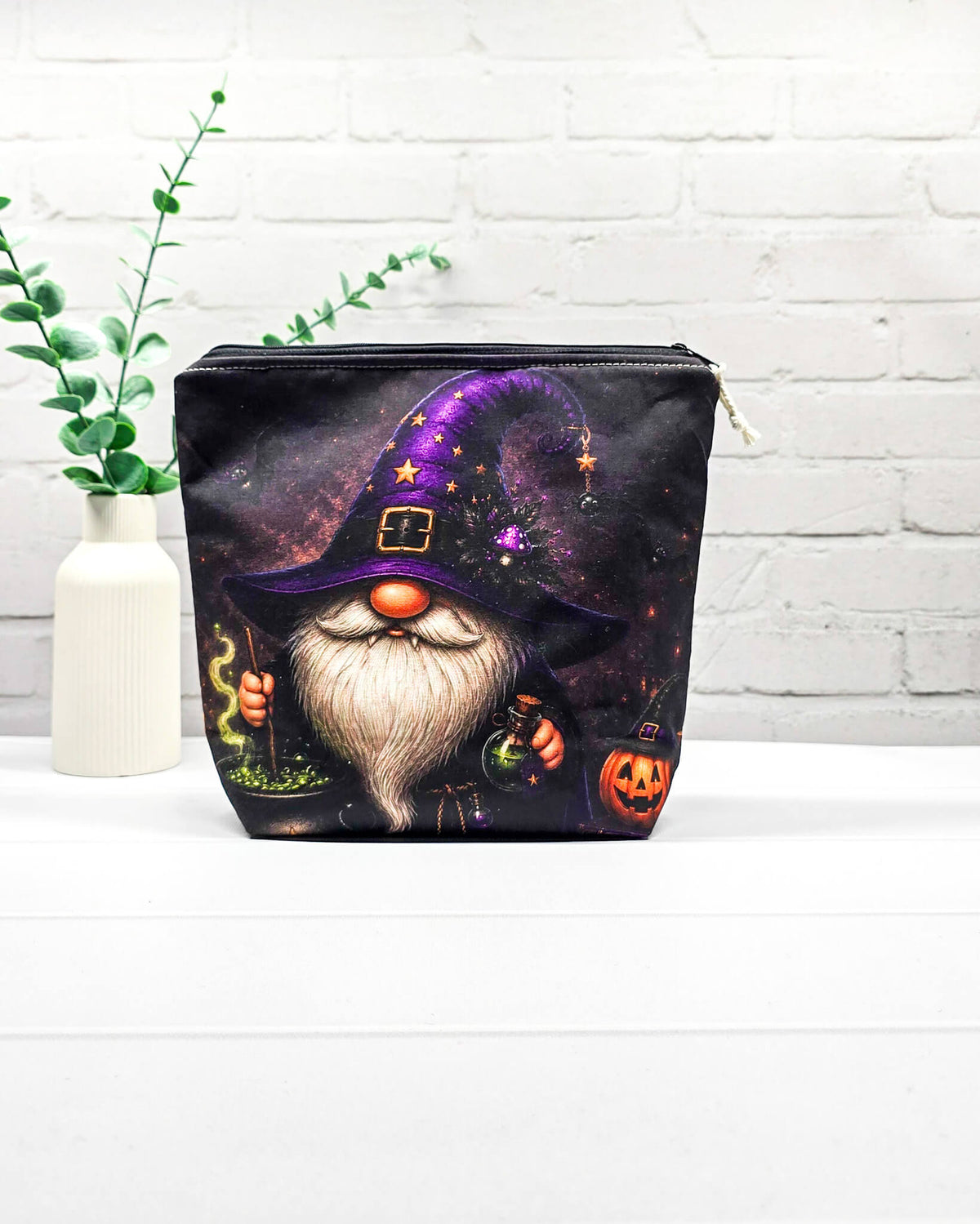 Projekttasche Isvind Größe S mit Halloweenwichtel, lila Hexenhut, weißem Bart, grün blubberndem Zaubertrank und orangefarbenem Kürbis auf dunklem Stoff. Mit Reißverschluss für kleine Strickprojekte. Handgenäht in Bayern von Nadelmikado.
