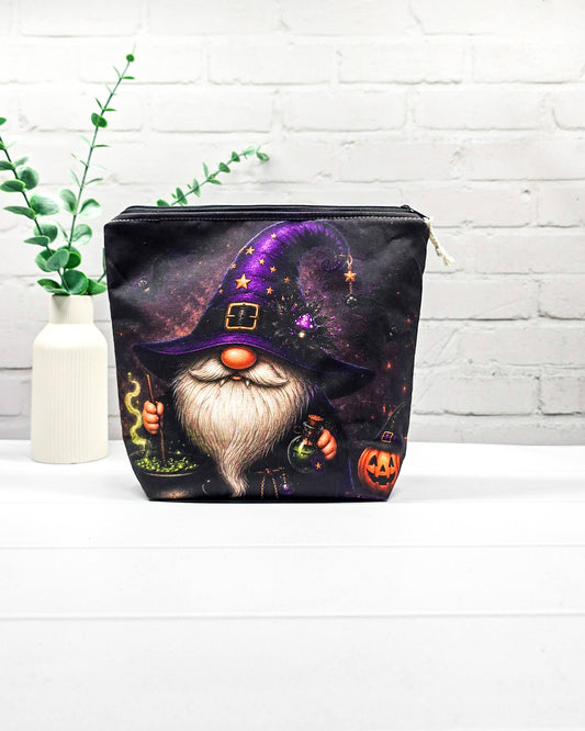 Projekttasche Isvind Größe S mit Halloweenwichtel, lila Hexenhut, weißem Bart, grün blubberndem Zaubertrank und orangefarbenem Kürbis auf dunklem Stoff. Mit Reißverschluss für kleine Strickprojekte. Handgenäht in Bayern von Nadelmikado.