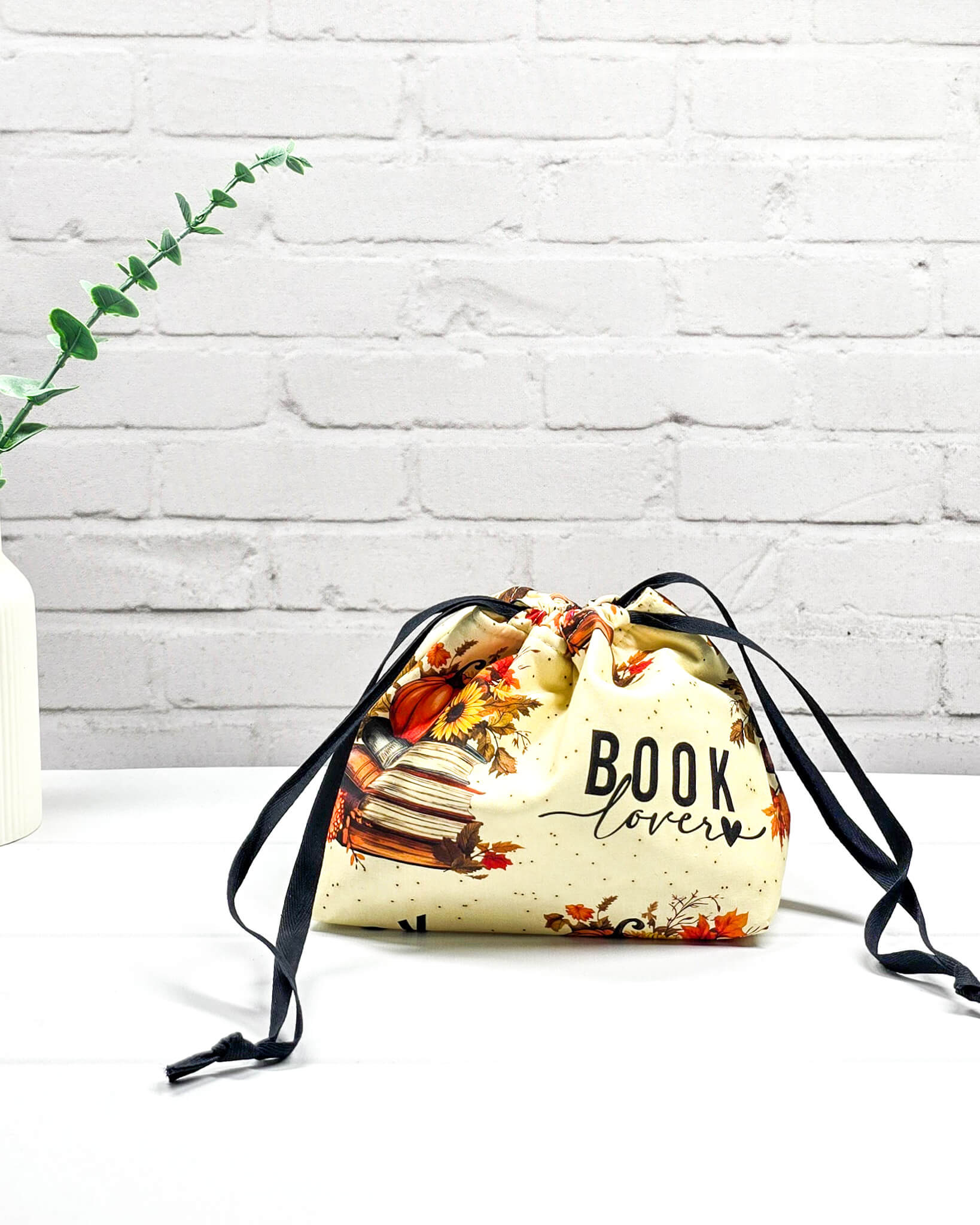 Projekttasche in Größe S für Sockenprojekte bis 100 g Wolle. Der Kinchaku-Verschluss bewahrt dein Strickzeug sicher auf. Motiv mit "Book Lover"-Schriftzug, Buchstapeln und herbstlichen Blumen. Handgenäht in Bayern von Nadelmikado