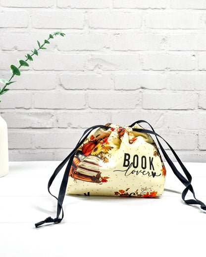 Projekttasche in Größe S für Sockenprojekte bis 100 g Wolle. Der Kinchaku-Verschluss bewahrt dein Strickzeug sicher auf. Motiv mit "Book Lover"-Schriftzug, Buchstapeln und herbstlichen Blumen. Handgenäht in Bayern von Nadelmikado