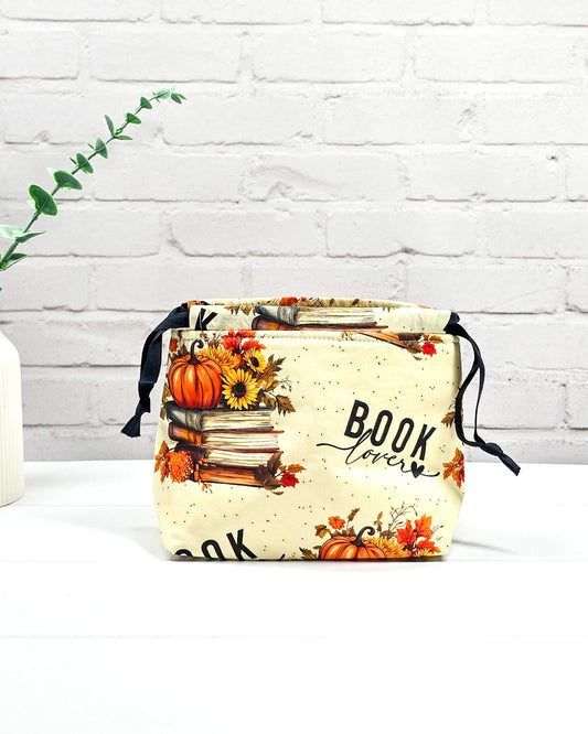 Projekttasche in Größe S für Sockenprojekte bis 100 g Wolle. Der Kinchaku-Verschluss bewahrt dein Strickzeug sicher auf. Motiv mit "Book Lover"-Schriftzug, Buchstapeln und herbstlichen Blumen. Handgenäht in Bayern von Nadelmikado