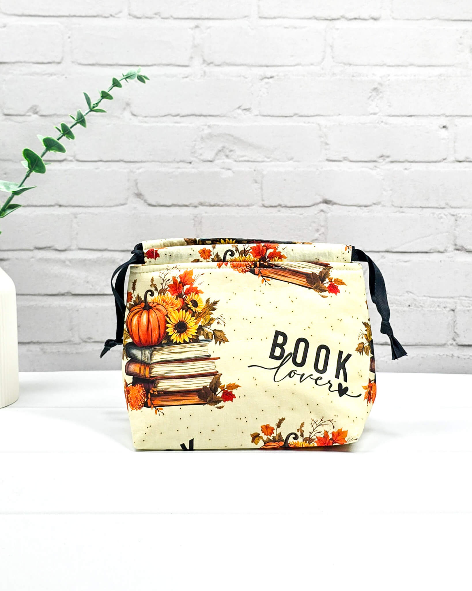 Projekttasche in Größe S für Sockenprojekte bis 100 g Wolle. Der Kinchaku-Verschluss bewahrt dein Strickzeug sicher auf. Motiv mit "Book Lover"-Schriftzug, Buchstapeln und herbstlichen Blumen. Handgenäht in Bayern von Nadelmikado
