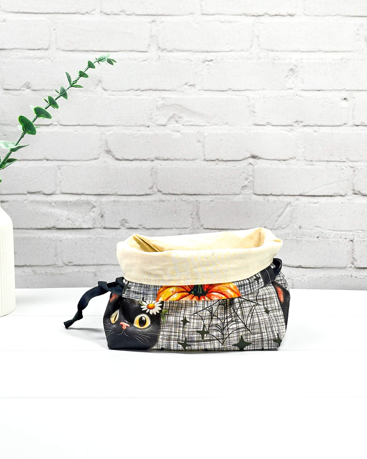 Projekttasche in Größe S für Sockenprojekte bis 100 g Wolle. Sicherer Kinchaku-Verschluss bewahrt das Strickzeug auf. Motiv mit schwarzer Katze, Blume am Ohr und Spinnennetz auf Karo-Grund. Handgenäht in Bayern von Nadelmikado
