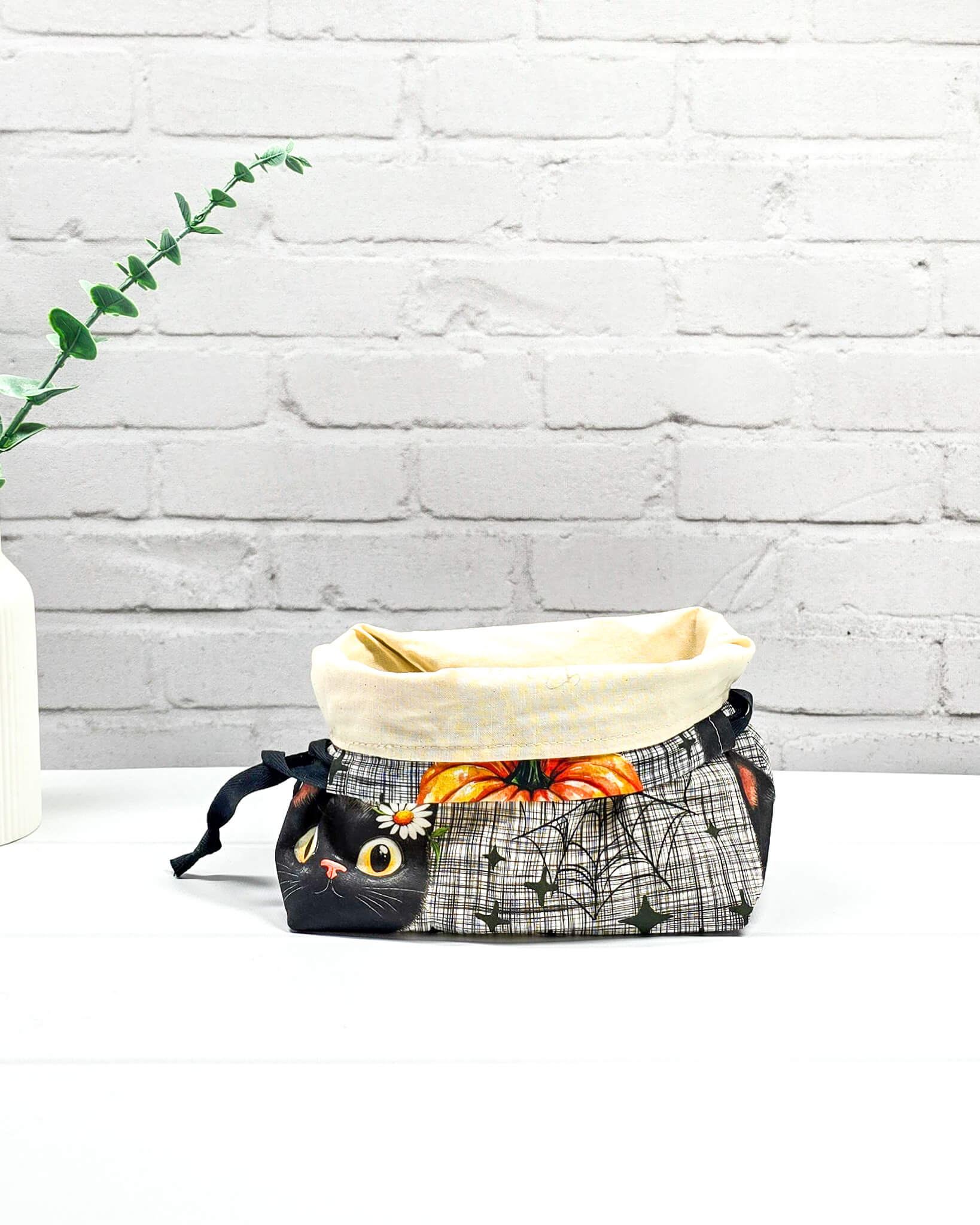 Projekttasche in Größe S für Sockenprojekte bis 100 g Wolle. Sicherer Kinchaku-Verschluss bewahrt das Strickzeug auf. Motiv mit schwarzer Katze, Blume am Ohr und Spinnennetz auf Karo-Grund. Handgenäht in Bayern von Nadelmikado