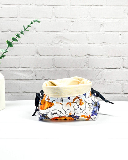 Projekttasche Lyra in Größe S im Kinchaku-Stil für Sockenprojekte bis 100 g Wolle. Motiv mit Kürbissen und violetten Blättern auf hellem Stoff und schwarzen Zugbändern. Handgenäht in Bayern von Nadelmikado