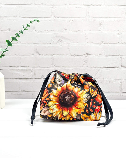 Projekttasche in Größe S für Sockenprojekte bis 100 g Wolle. Kinchaku-Verschluss sichert das Strickzeug. Motiv mit großer Sonnenblume und Herbstlaub auf dunklem Stoff. Handgenäht in Bayern von Nadelmikado. 