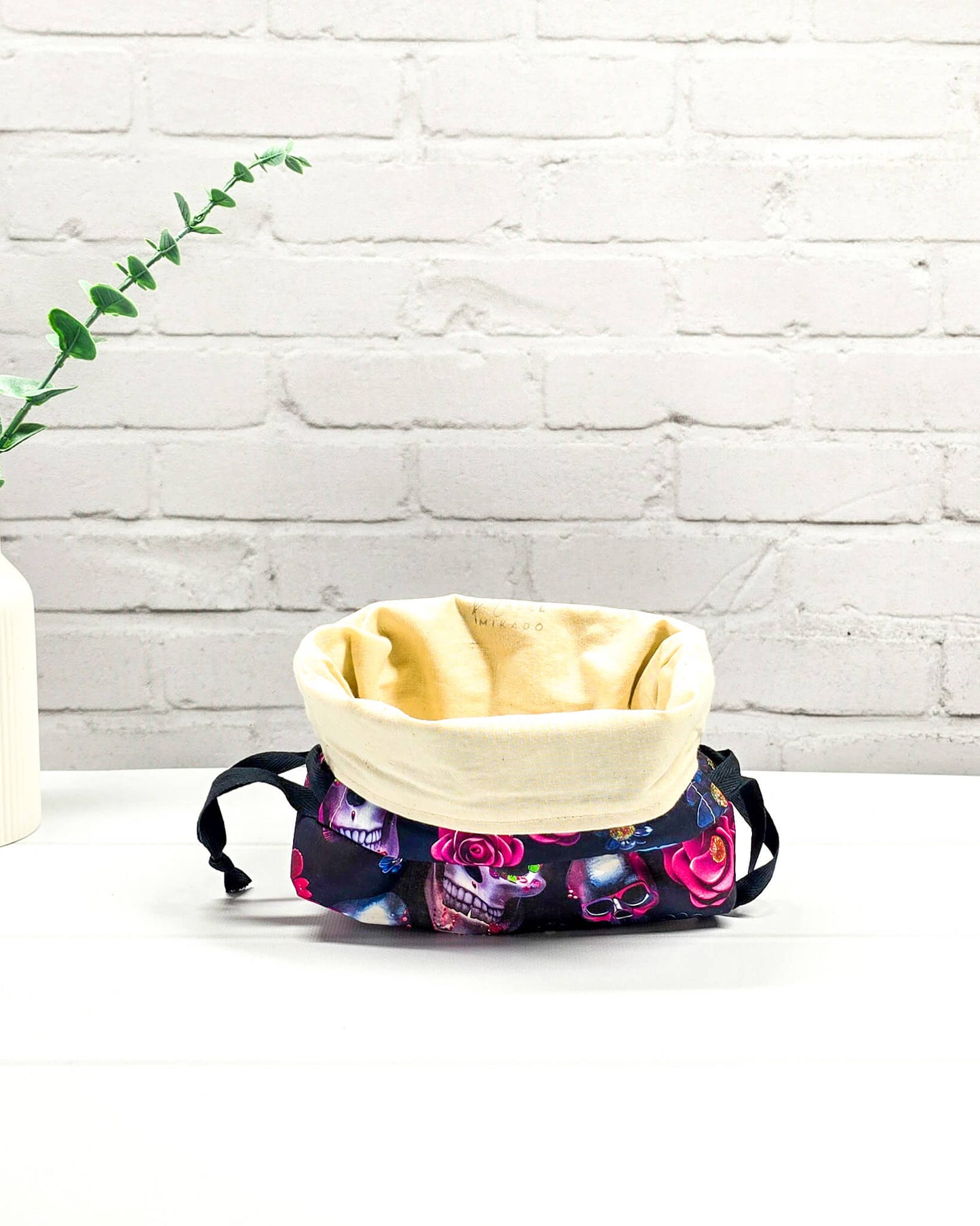 Projekttasche in Größe S für Sockenprojekte bis 100 g Wolle. Sicherer Kordelzug-Verschluss bewahrt das Strickzeug auf. Motiv mit verzierten Totenschädeln und pinken Rosen auf dunklem Stoff. Handgenäht in Bayern von Nadelmikado