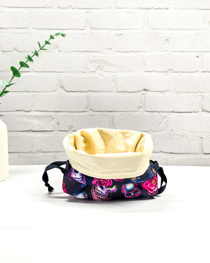 Projekttasche in Größe S für Sockenprojekte bis 100 g Wolle. Sicherer Kordelzug-Verschluss bewahrt das Strickzeug auf. Motiv mit verzierten Totenschädeln und pinken Rosen auf dunklem Stoff. Handgenäht in Bayern von Nadelmikado