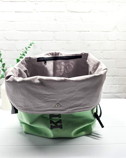Projekttasche Rika im Roll-Top-Design aus hellgrünem Canvas mit vertikalem, dunkelgrauem Schriftzug „KNITTING“ und schwarzem Gurtband-Verschluss. Handgenäht in Bayern von Nadelmikado. 