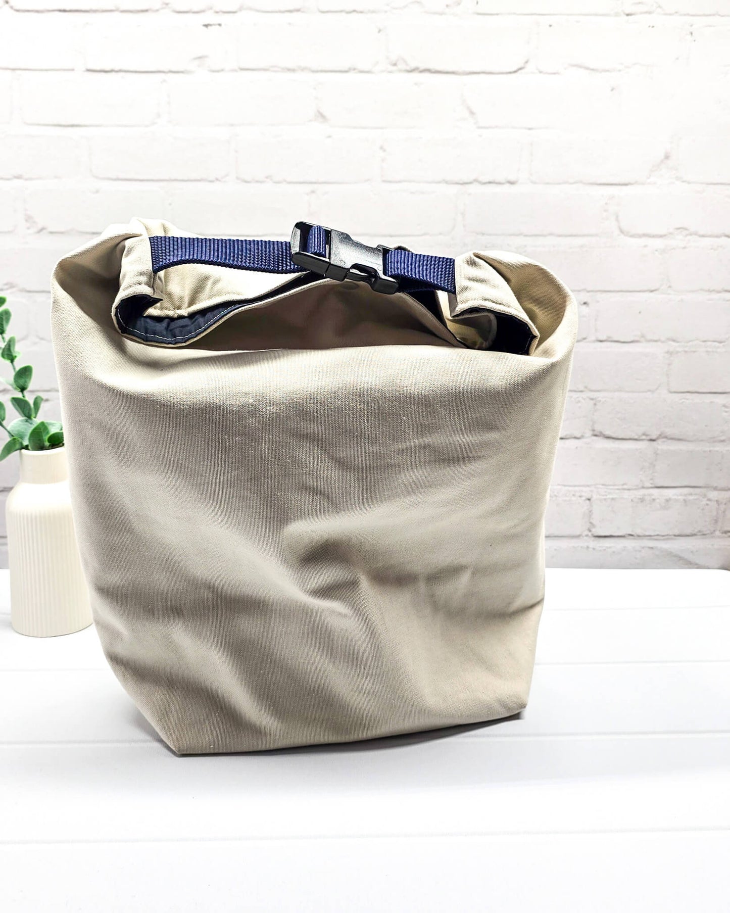 Projekttasche Rika im Roll-Top-Design aus naturfarbenem Canvas mit vertikalem, dunkelblauem Schriftzug „KNITTING“ und blauem Gurtband-Verschluss. Handgenäht in Bayern von Nadelmikado. 
