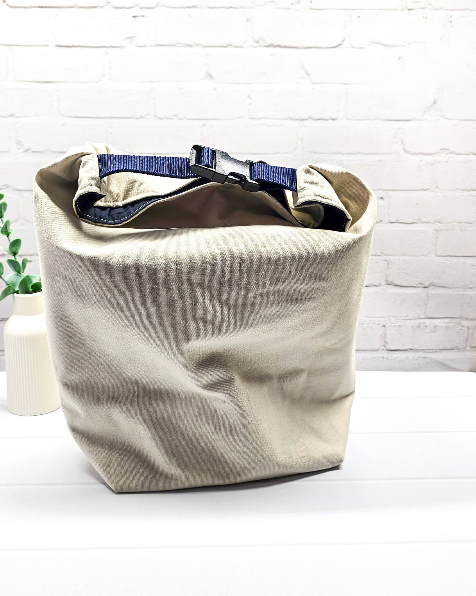 Projekttasche Rika im Roll-Top-Design aus naturfarbenem Canvas mit vertikalem, dunkelblauem Schriftzug „KNITTING“ und blauem Gurtband-Verschluss. Handgenäht in Bayern von Nadelmikado. 