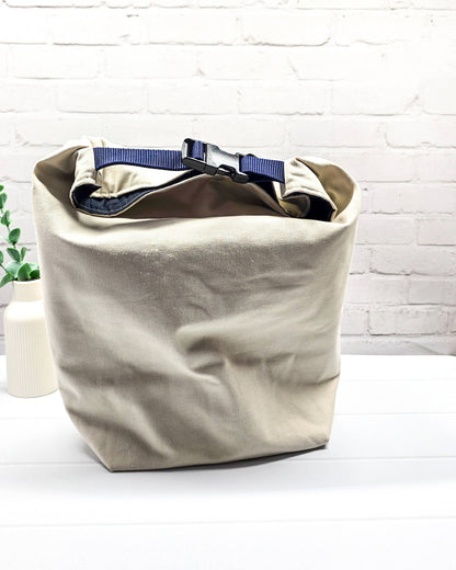 Projekttasche Rika im Roll-Top-Design aus naturfarbenem Canvas mit vertikalem, dunkelblauem Schriftzug „KNITTING“ und blauem Gurtband-Verschluss. Handgenäht in Bayern von Nadelmikado. 