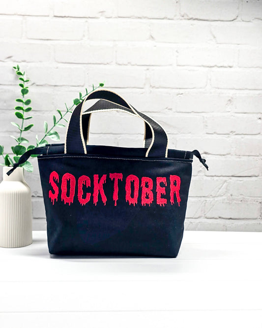 Projekttasche Alva S aus schwarzem Canvas mit leuchtend rotem Socktober-Schriftzug, handgenäht und bestickt in Bayern von NadelMikado