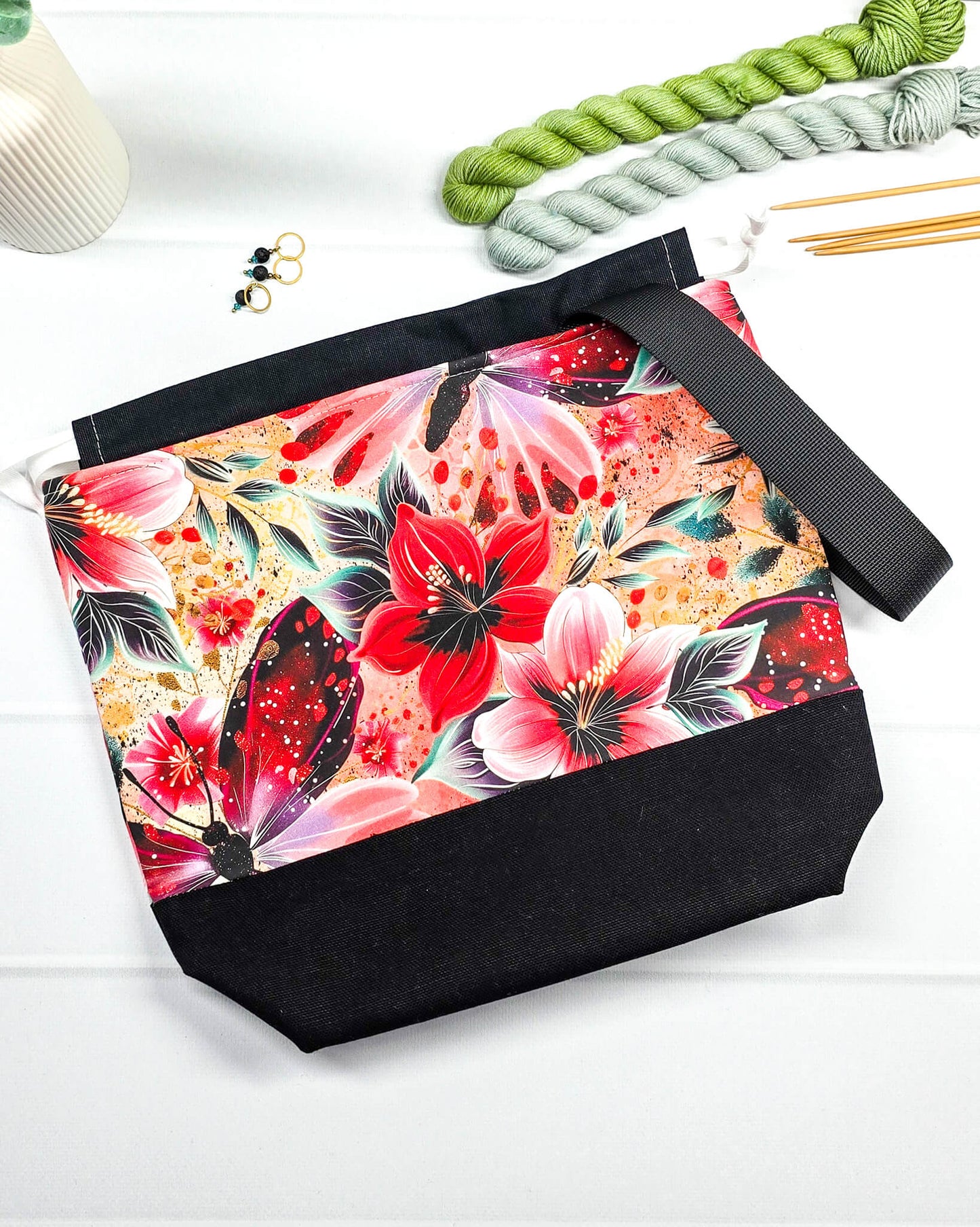 Handgenähte Projekttasche mit leuchtend roten Blüten und Schmetterlingen auf dunklem Grund mit schwarzem Boden. Handmade in Bayern von Nadelmikado.