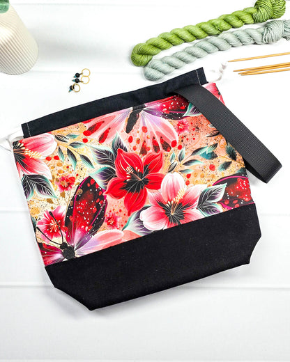 Handgenähte Projekttasche mit leuchtend roten Blüten und Schmetterlingen auf dunklem Grund mit schwarzem Boden. Handmade in Bayern von Nadelmikado.