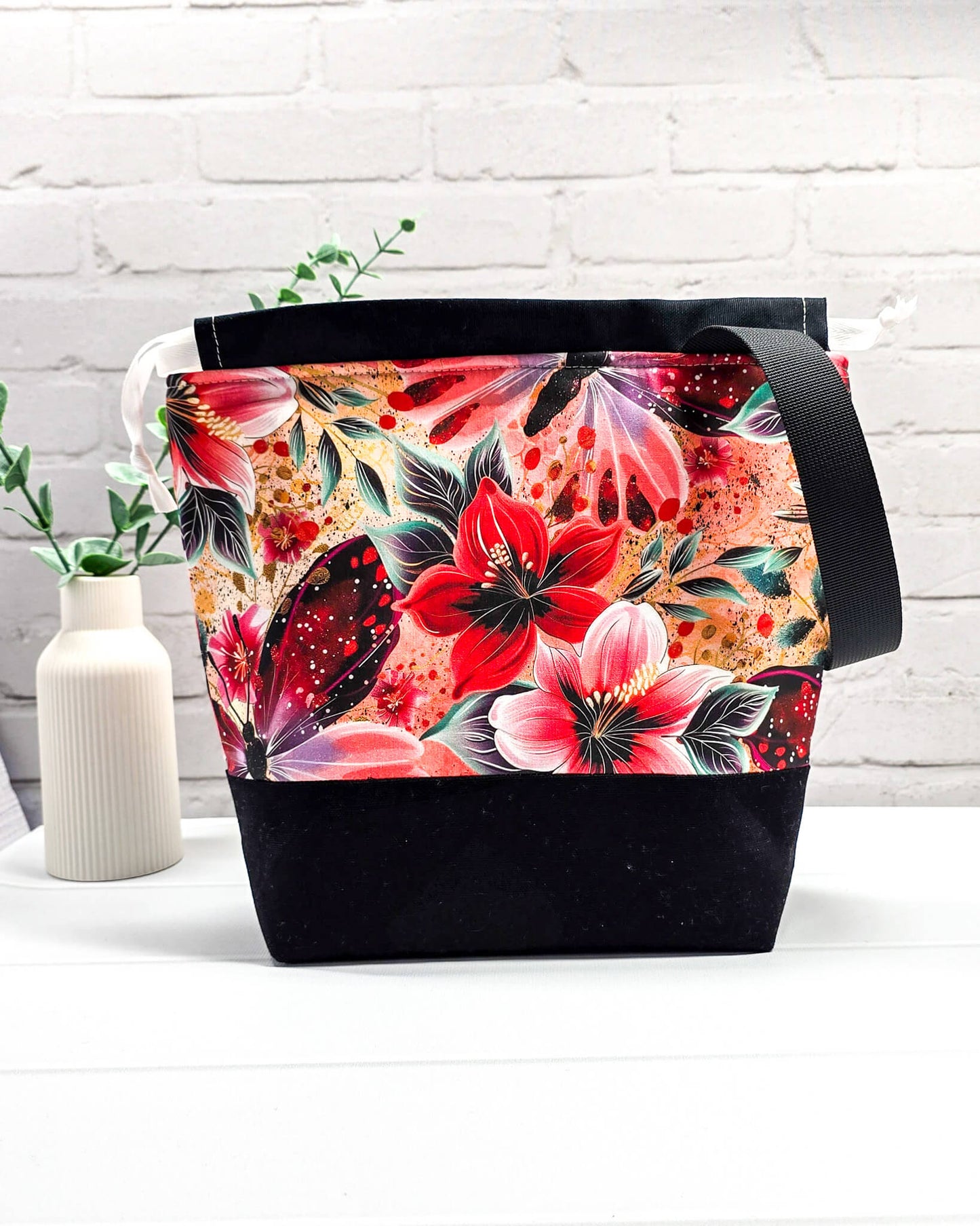 Handgenähte Projekttasche mit leuchtend roten Blüten und Schmetterlingen auf dunklem Grund mit schwarzem Boden. Handmade in Bayern von Nadelmikado.